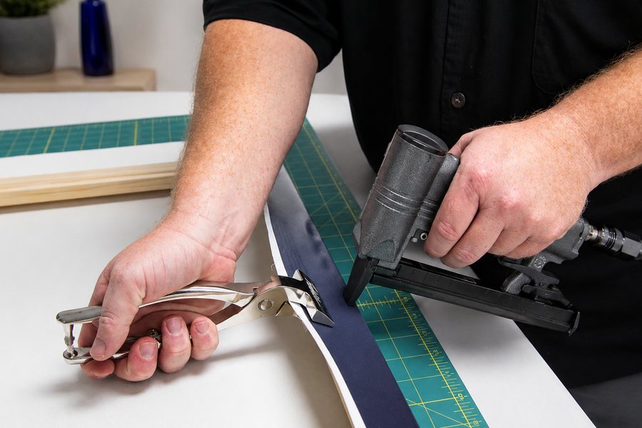 Hands stretching a printed canvas over a wooden stretcher bar and securing it with a staple gun.